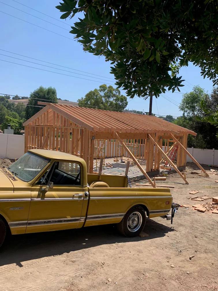 House framing in progress with a yellow vintage pickup truck parked in front.