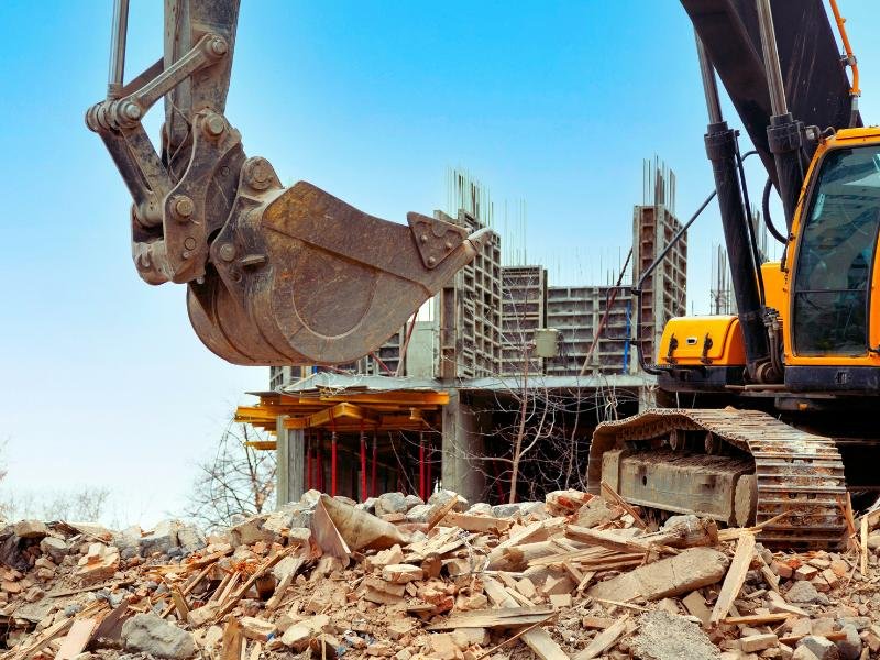 Heavy machinery demolishing a building, with debris scattered around the site.