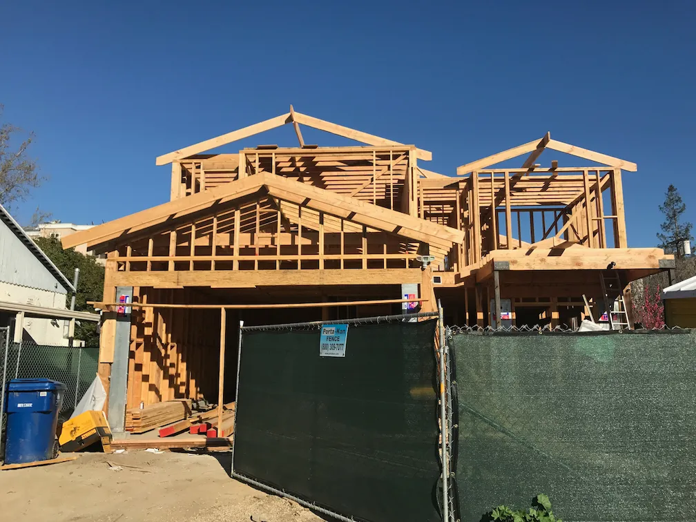 House framing in progress with a green gate partially obstructing the view.
