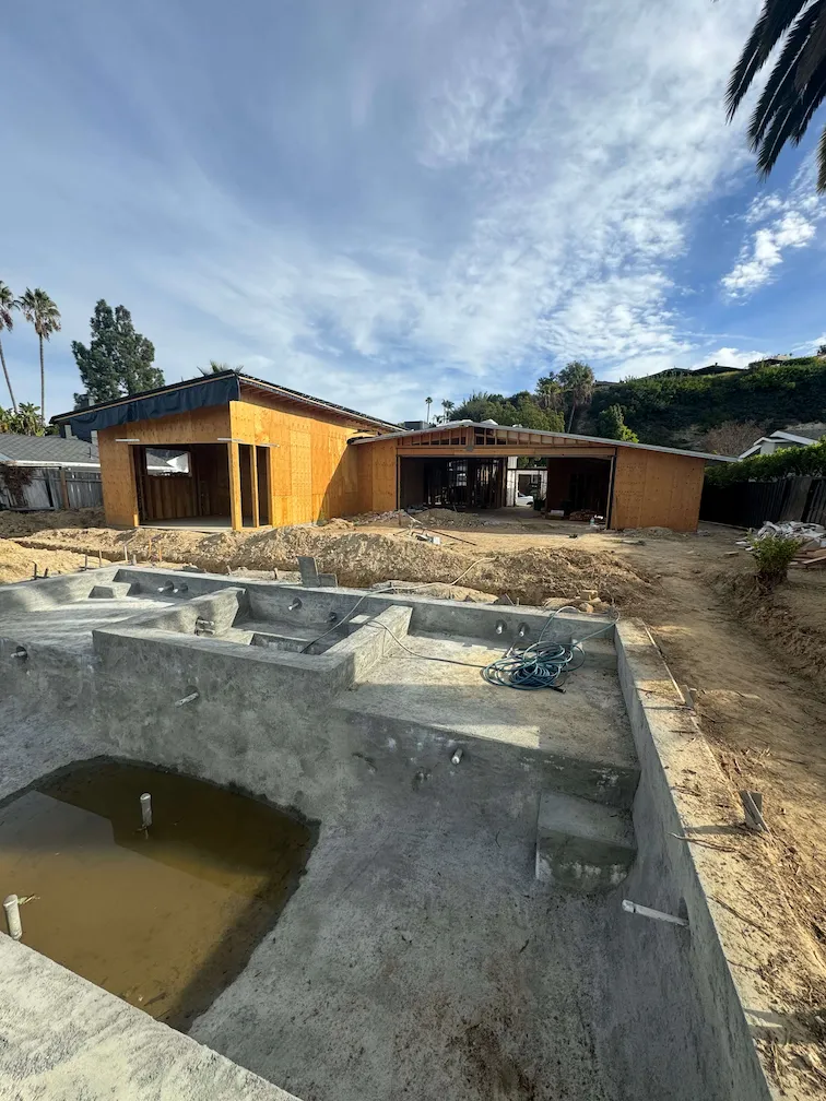 House under construction with nearly completed framing, an empty pool, and dirt-covered surroundings.