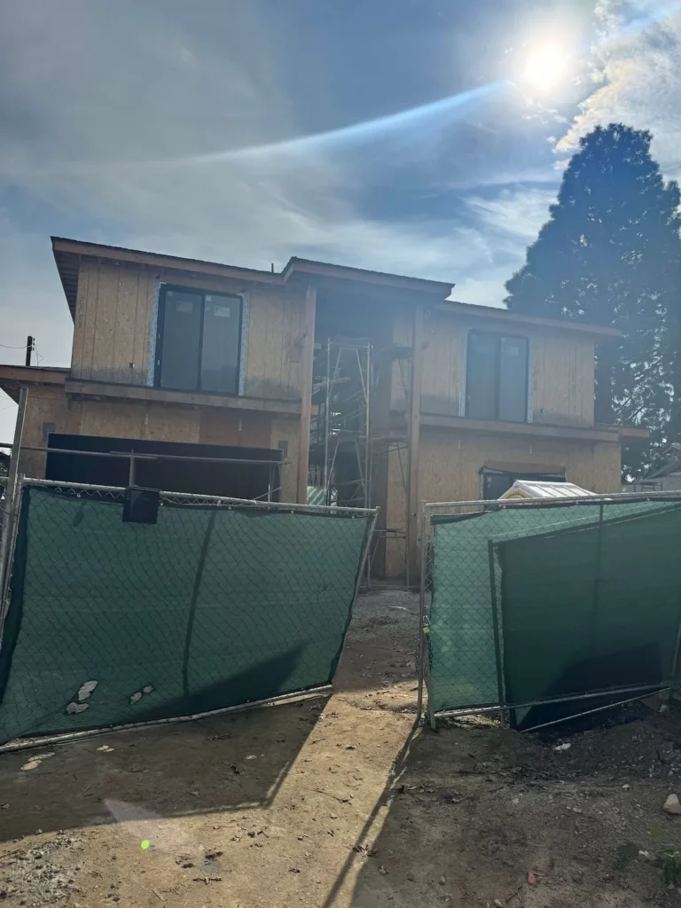 House framing in progress with installed windows and a green gate in the front.