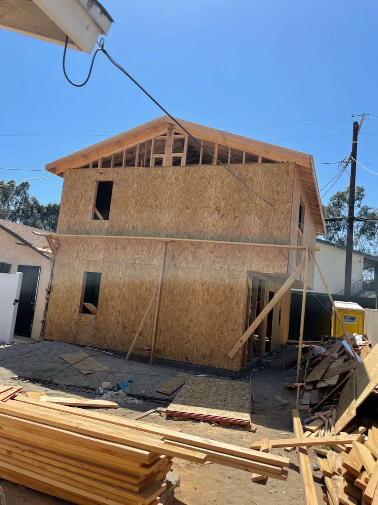Framing in progress for a new house, surrounded by stacks of wood and construction materials.