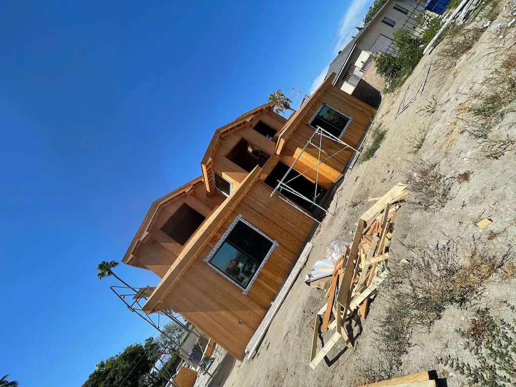 Completed framing for a newly built house with installed windows, wood materials, and dirt in the front.