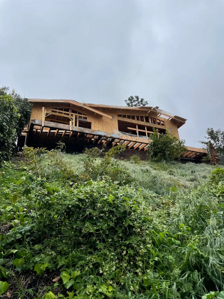 Framing job in progress on a house above a hill, with a greenery-covered slope in the foreground.