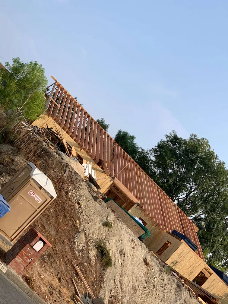 Framing in progress with a focus on the house's roof, with a tan Porta Potty visible in the image.