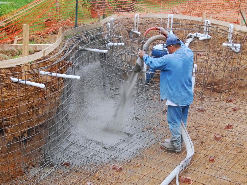 Construction worker pouring cement into an unfinished pool.