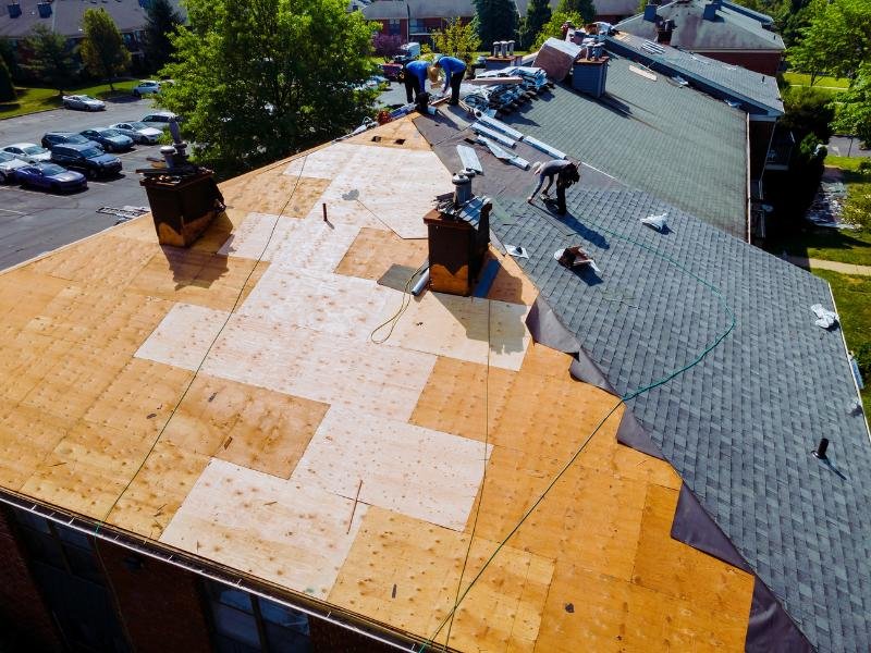 Construction workers installing shingles on a partially completed roof.