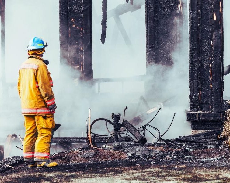 Firefighter observing the aftermath of a burnt-down building.