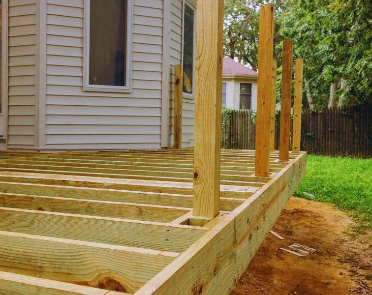 Backyard patio construction in progress with wooden framing attached to the house.