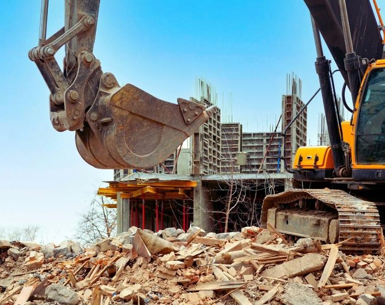 Heavy machinery demolishing a building, with debris scattered around the site.