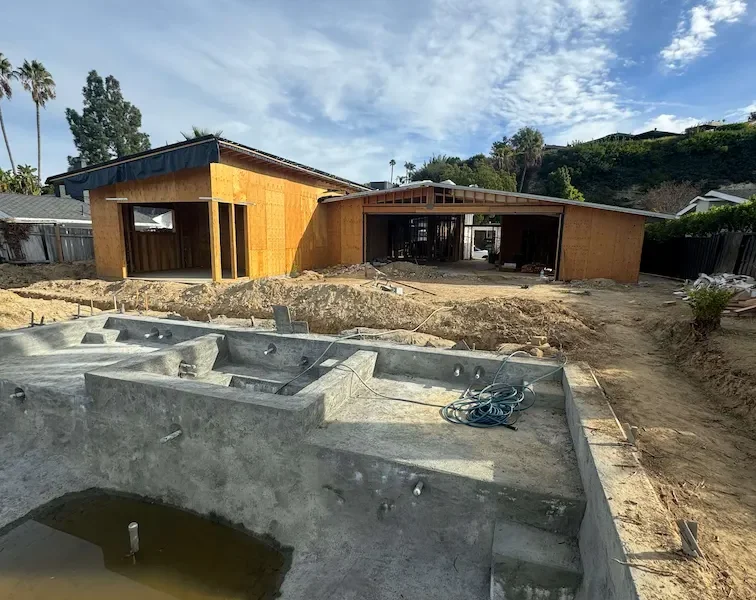 House under construction with nearly completed framing, an empty pool, and dirt-covered surroundings.