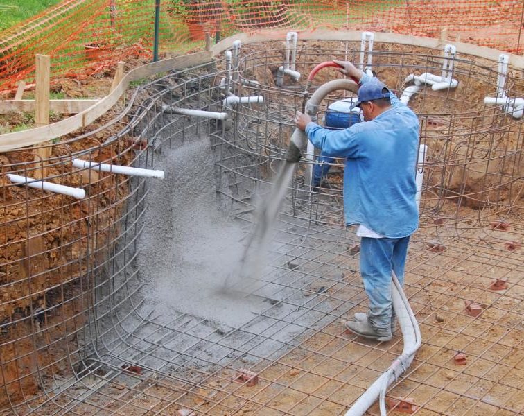 Construction worker pouring cement into an unfinished pool.