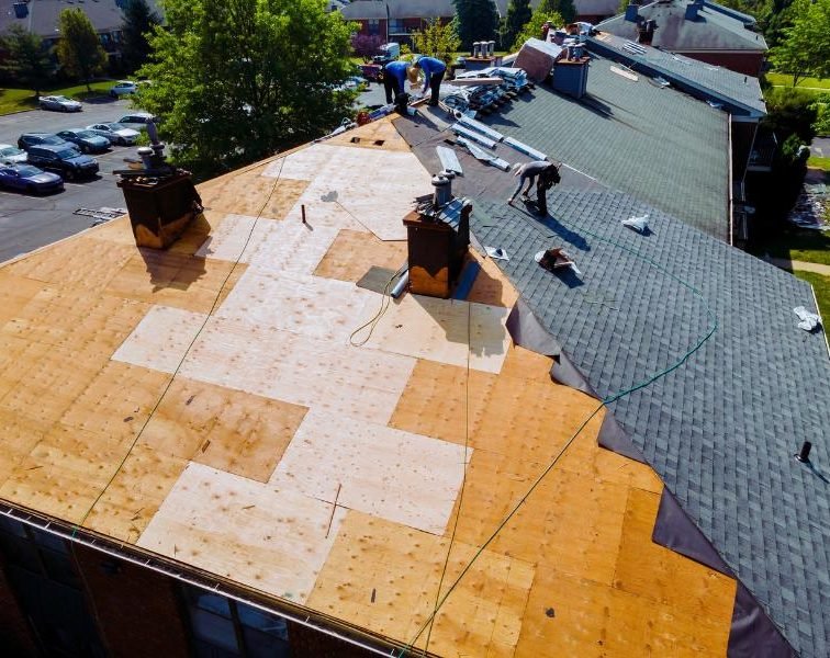 Construction workers installing shingles on a partially completed roof.